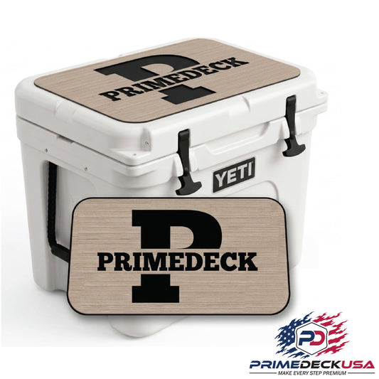 White Yeti cooler with custom beige wood-grain branded covers on the lid and front, featuring a large black 'P' and 'PRIMEDECK' text. A matching rectangular mat is shown in front on a white background with a PrimeDeckUSA logo in the bottom right corner.