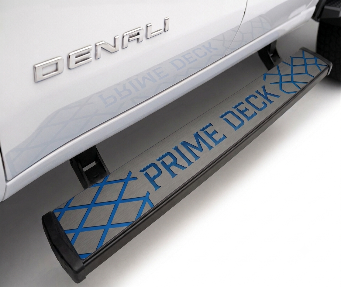 A close-up of a black and gray running deck with blue 'PRIME DECK' lettering and a blue diamond pattern, mounted on the side of a white Denali vehicle.